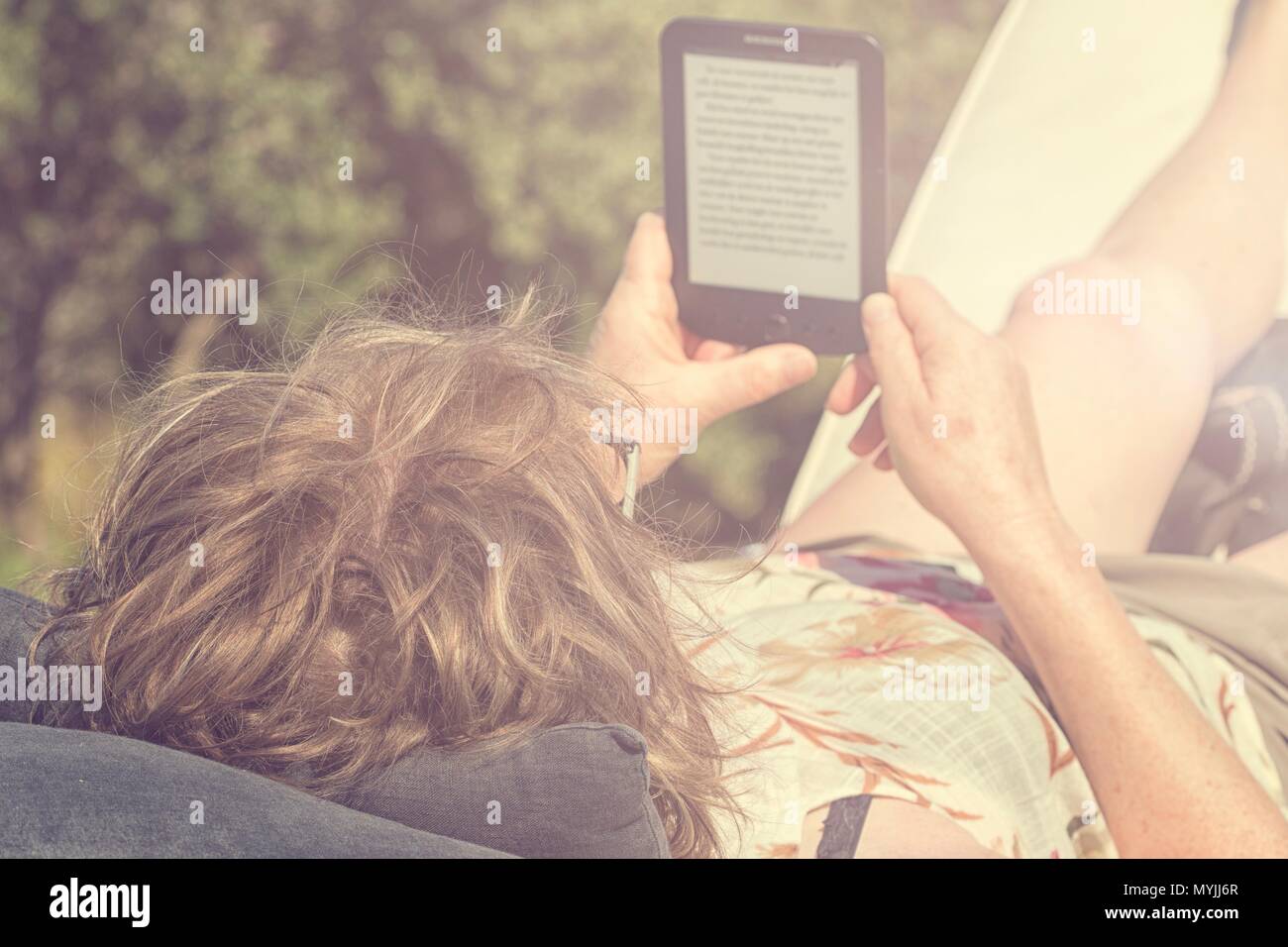 Donna sdraiata sulla sedia a sdraio di lettura di un ebook sotto il sole Foto Stock