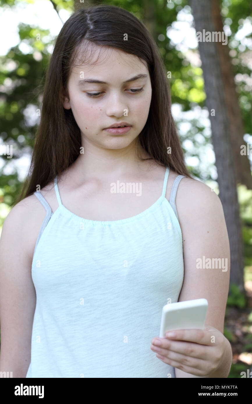 Preoccupato ferire giovane ragazza adolescente la lettura di un messaggio di testo sullo smartphone. Messa a fuoco selettiva su teen. Foto Stock