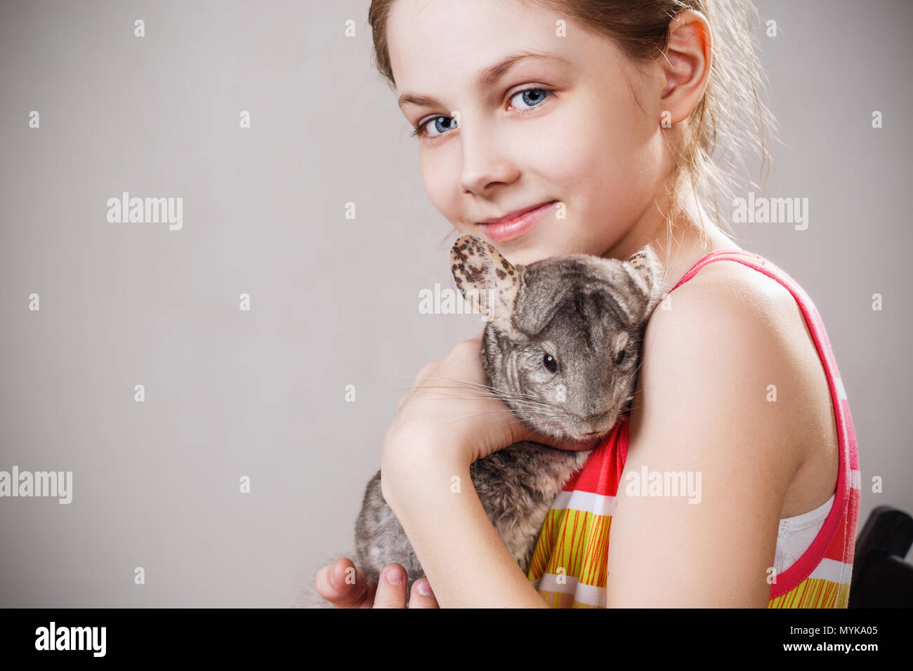 Carino sorridente bambina detiene funny grigio chinchilla. Foto Stock