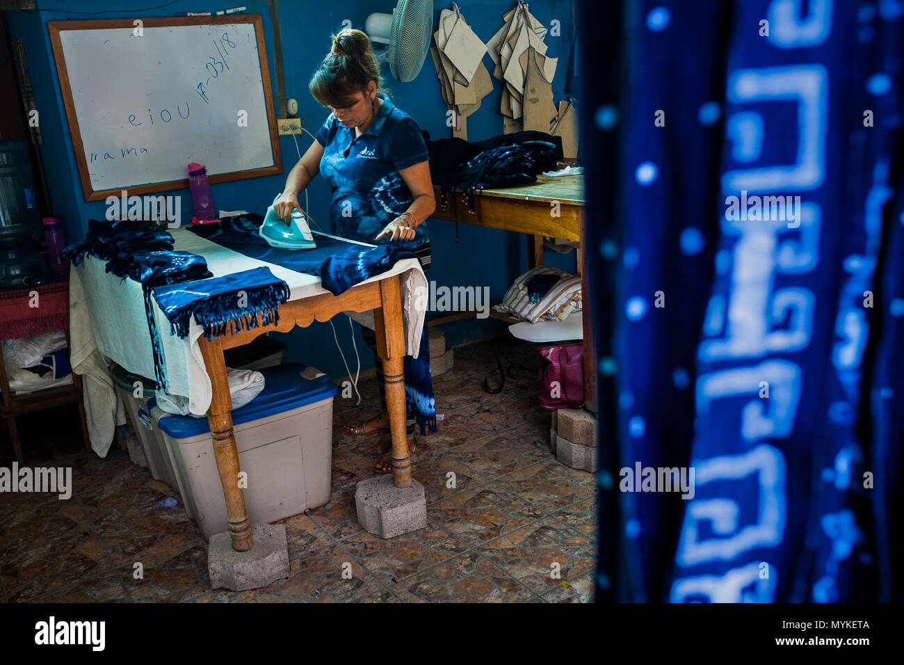 Una donna di Salvadoran ferri da stiro indaco-tinto vestito in un abbigliamento artigianale laboratorio in Santiago Nonualco, El Salvador. Foto Stock