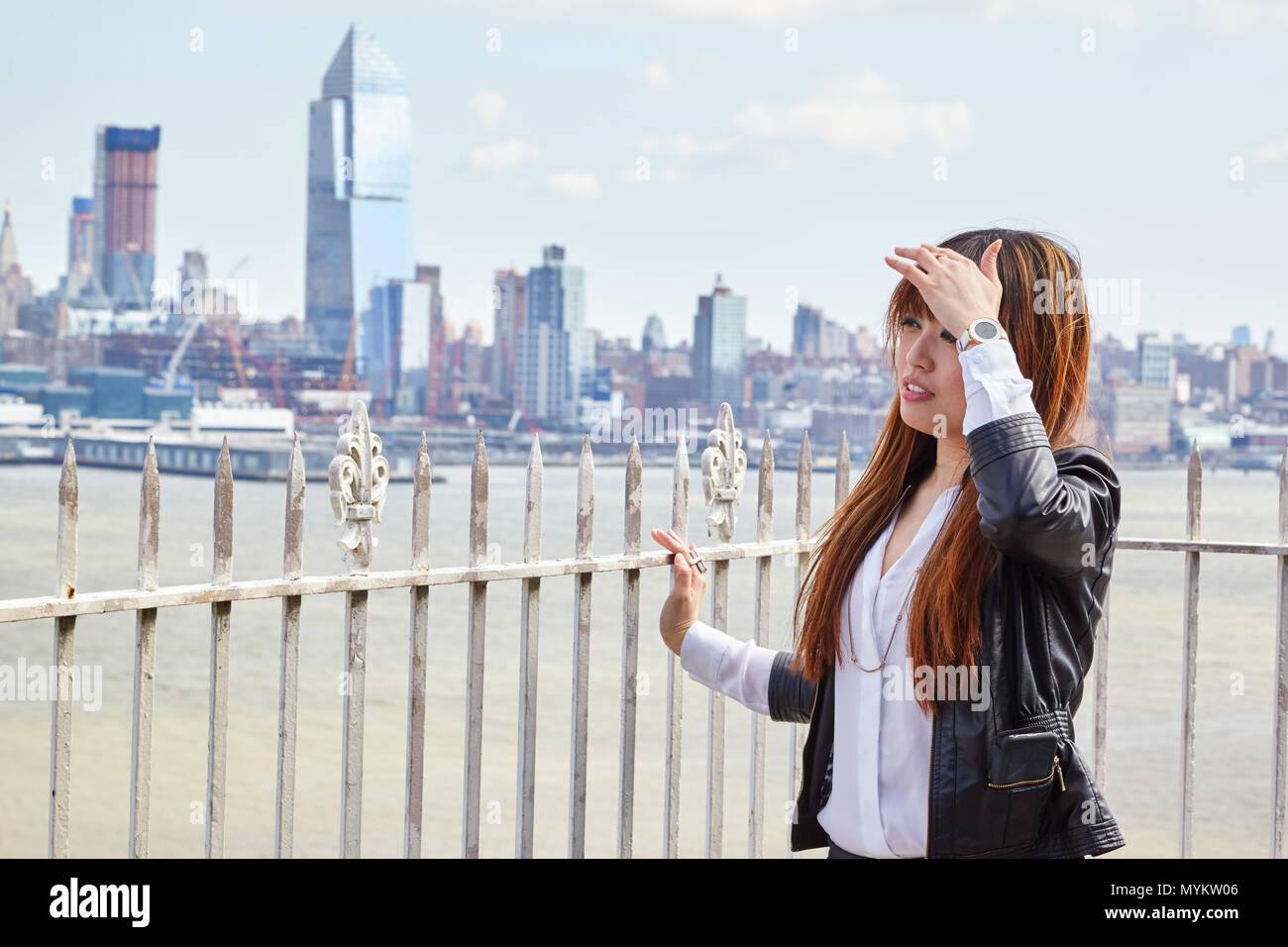 Donna asiatica in giacca di pelle in piedi di fronte a skyline della città Foto Stock