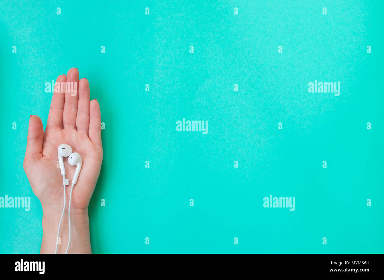 Signora della mano con bella manicure holding auricolari su 'turqoise' colore di sfondo. Foto Stock