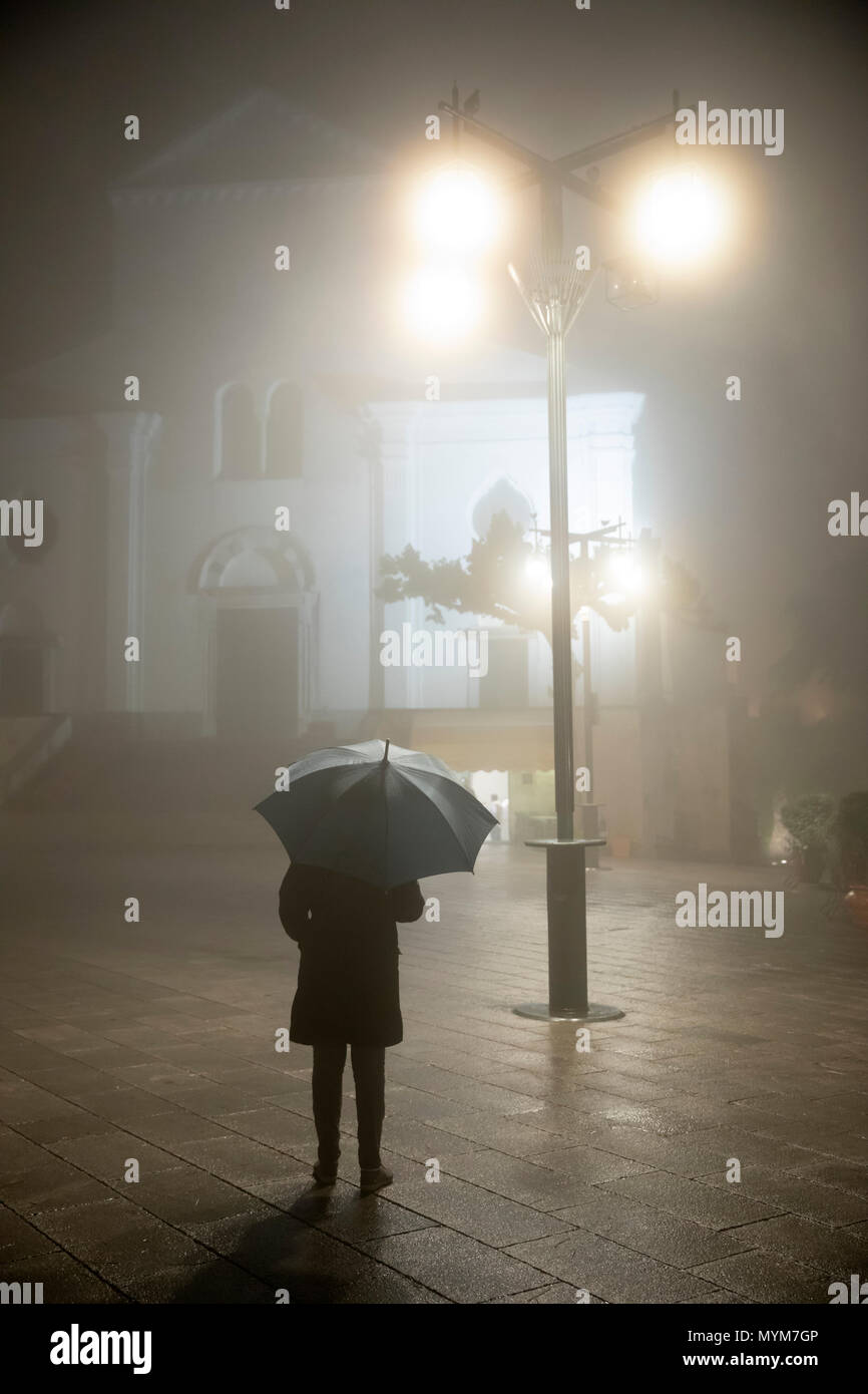 Persona con ombrellone in piedi sotto il lampione di fronte al duomo di pioggia e nebbia di notte, Ravello, la Costiera Amalfitana, Campania, Italia, Europa Foto Stock