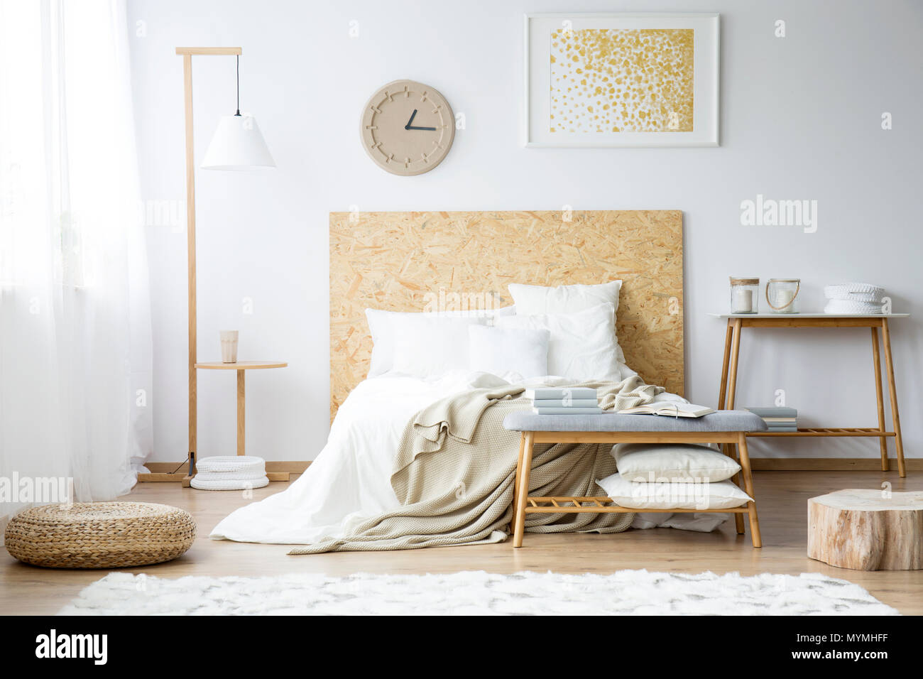 Orologio di carta oro e dipinto sulla parete sopra il letto con lenzuola di  color beige in camera da letto con pouf e mobili in legno Foto stock - Alamy