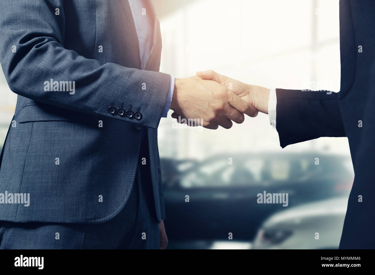 Venditore e handshake del cliente dopo aver eseguito correttamente la trattativa in concessionaria auto Foto Stock