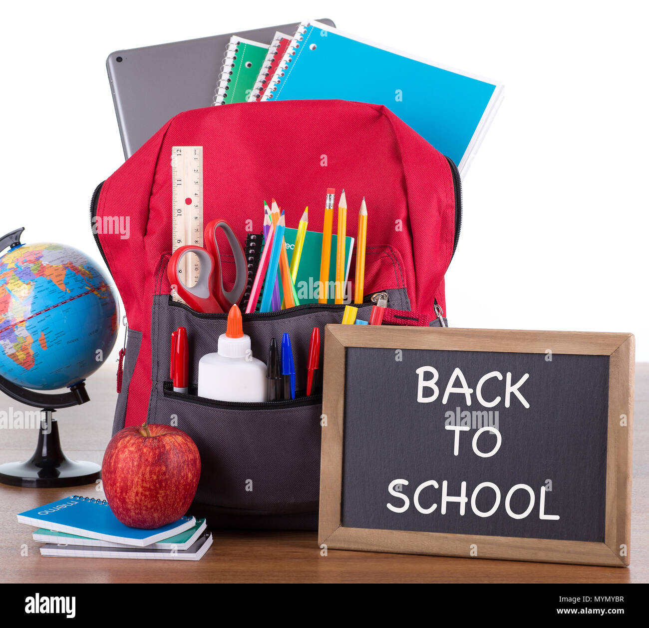 Zaino con un vasto assortimento di forniture scolastiche con il ritorno a scuola scritto su una lavagna su una scrivania in legno e sfondo bianco Foto Stock