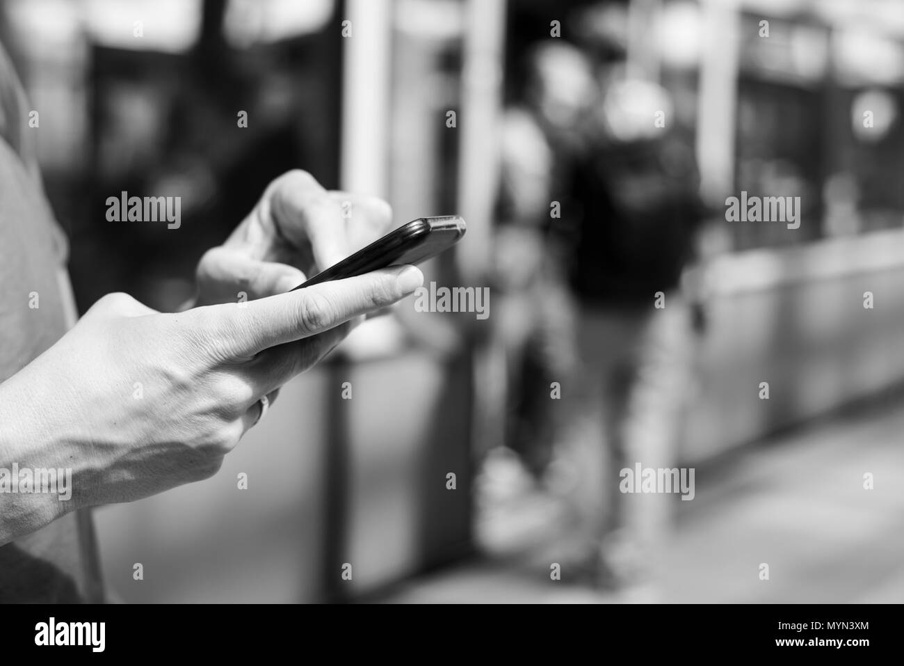Primo piano di un giovane uomo caucasico utilizzando uno smartphone in un treno della metropolitana o tram stazione, in bianco e nero Foto Stock