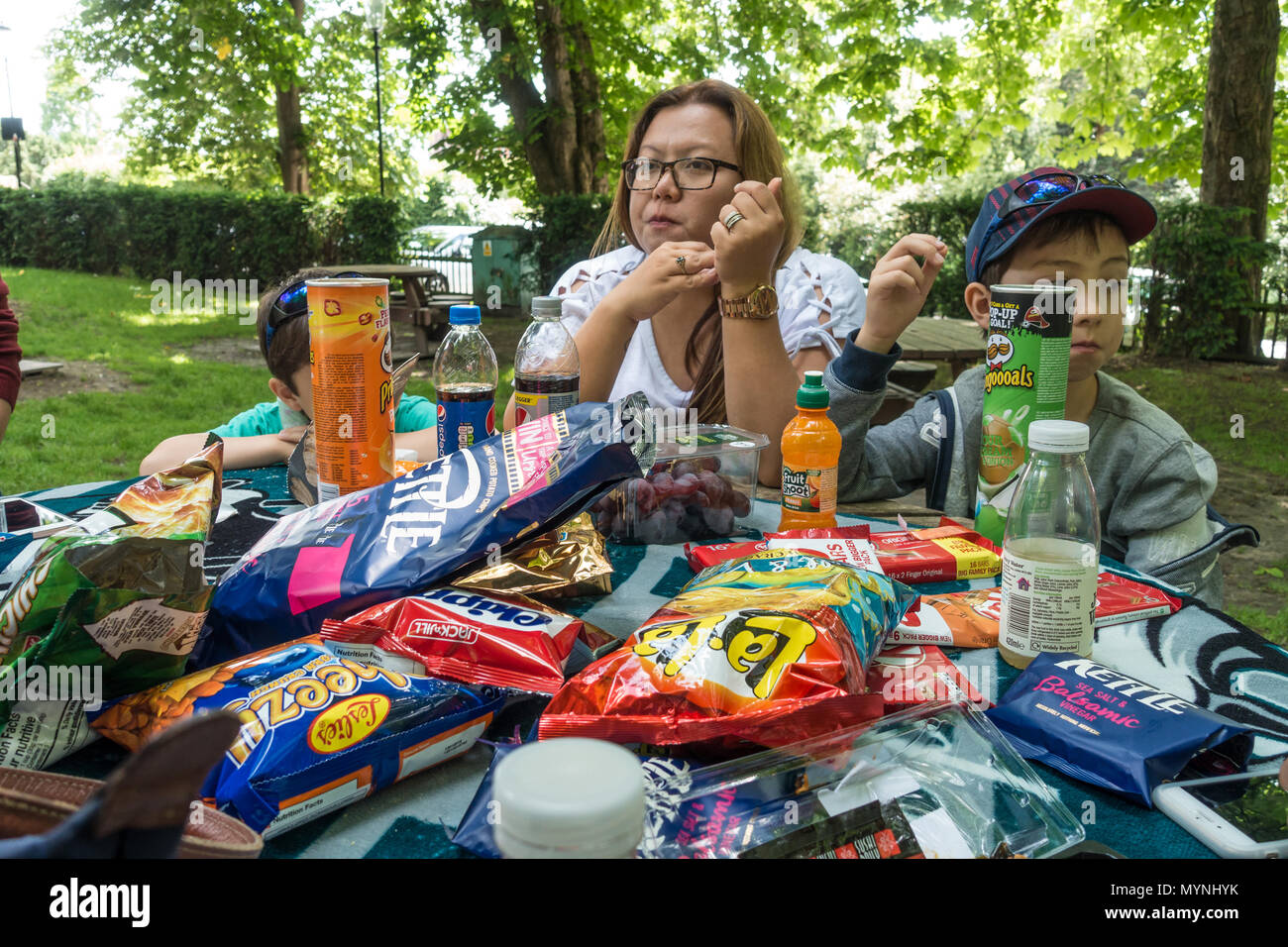 Una madre e figli sedersi a un tavolo da picnic coperta in pacchetti dei Crips e altri snack. Foto Stock