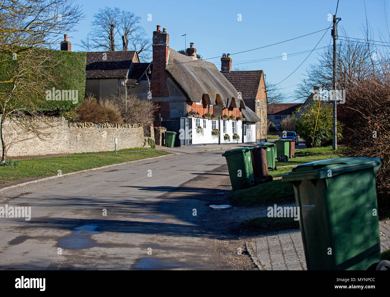 Church Street, West Hanney, Oxfordshire, Regno Unito. Scomparti Wheelie attendono lo svuotamento in primo piano con il XVII secolo Plough Inn in background. Foto Stock