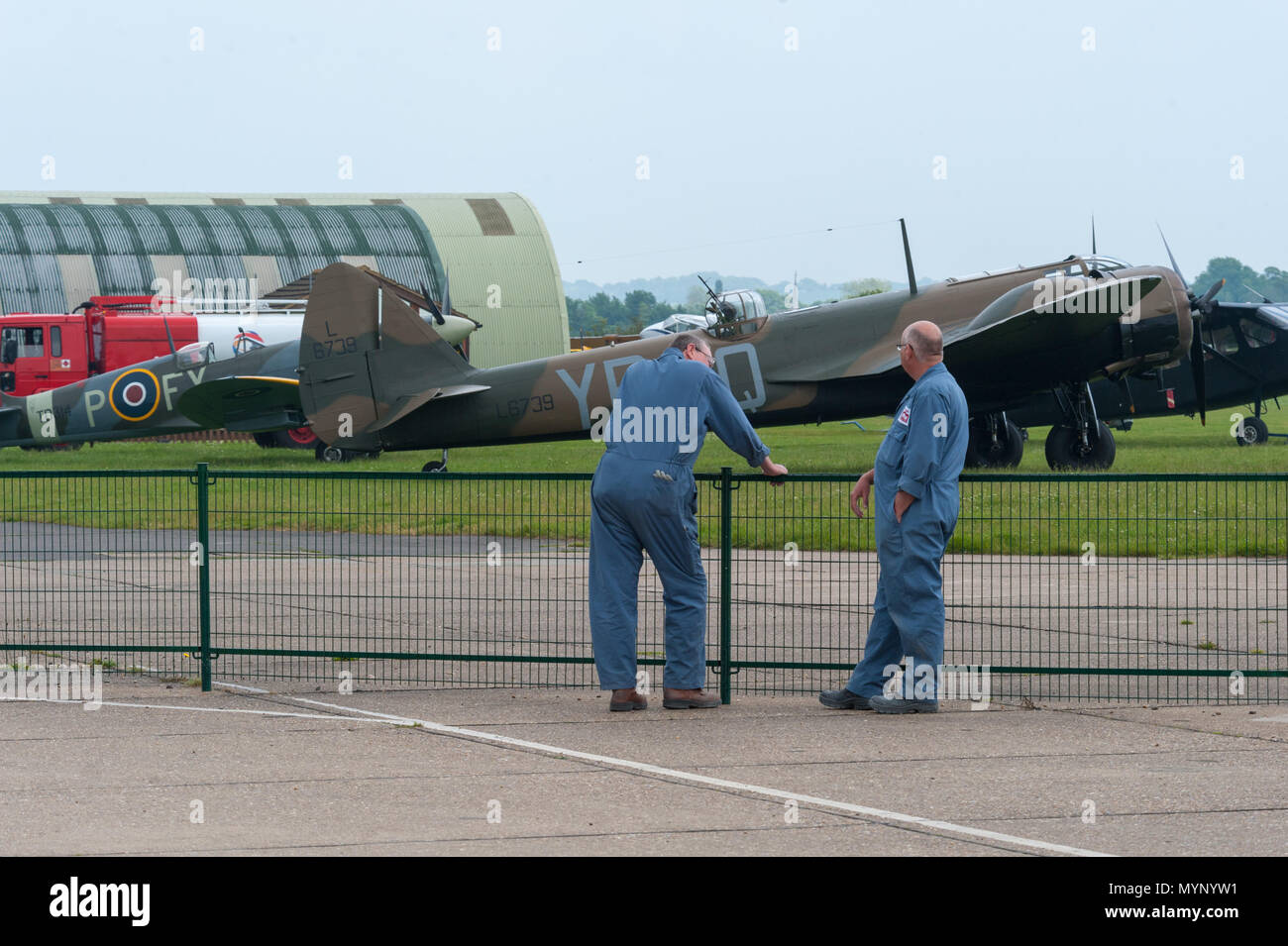 Due membri dell'equipaggio di terra in tuta blu riposano vicino a un bombardiere d'epoca della seconda guerra mondiale della RAF in un aeroporto durante uno storico evento di aviazione in Inghilterra Foto Stock