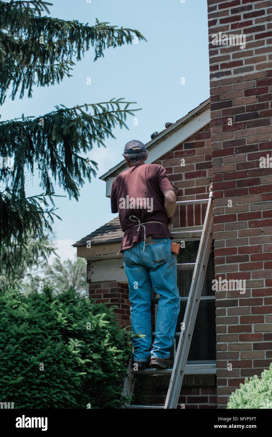 Un uomo su una scala, lavorando per la riparazione di una casa di mattoni Foto Stock
