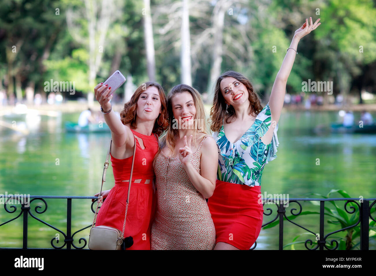 Tre ragazze, amici, sorridere e prendere un selfie insieme. La ragazza bionda winks e con le sue dita rende il segno della vittoria. Sullo sfondo la gr Foto Stock