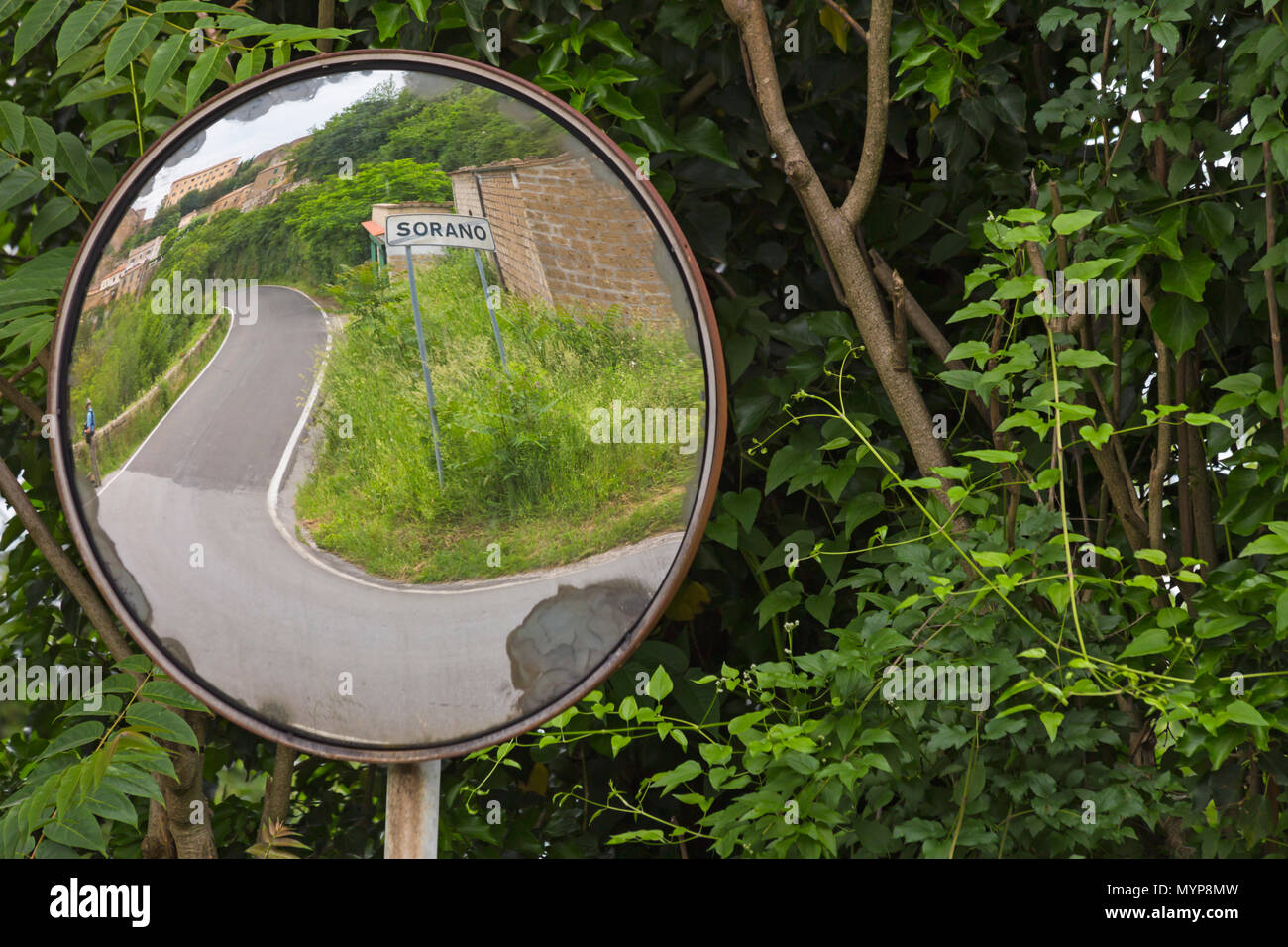 Vista attraverso specchio rotondo di strada tortuosa per l'antico borgo medioevale città di collina Sorano, Toscana, Italia nel mese di maggio Foto Stock