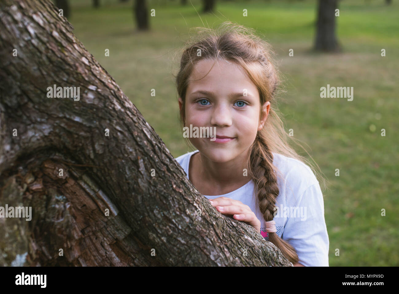 Giocoso bambino bambina che si nasconde dietro la grande tronco di albero da estate Foto Stock