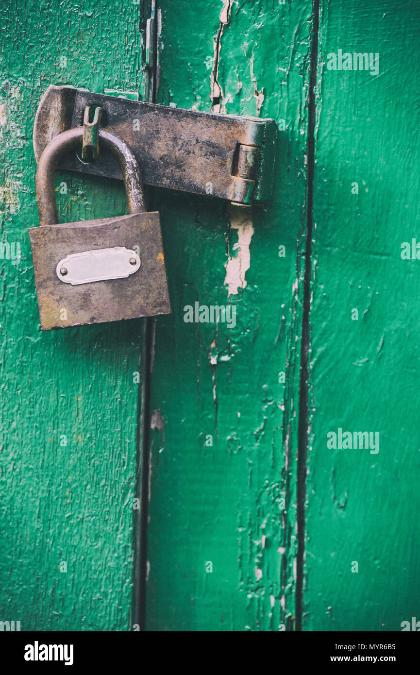 Bloccato il lucchetto arrugginito su un weathered casottino verde porta Foto Stock