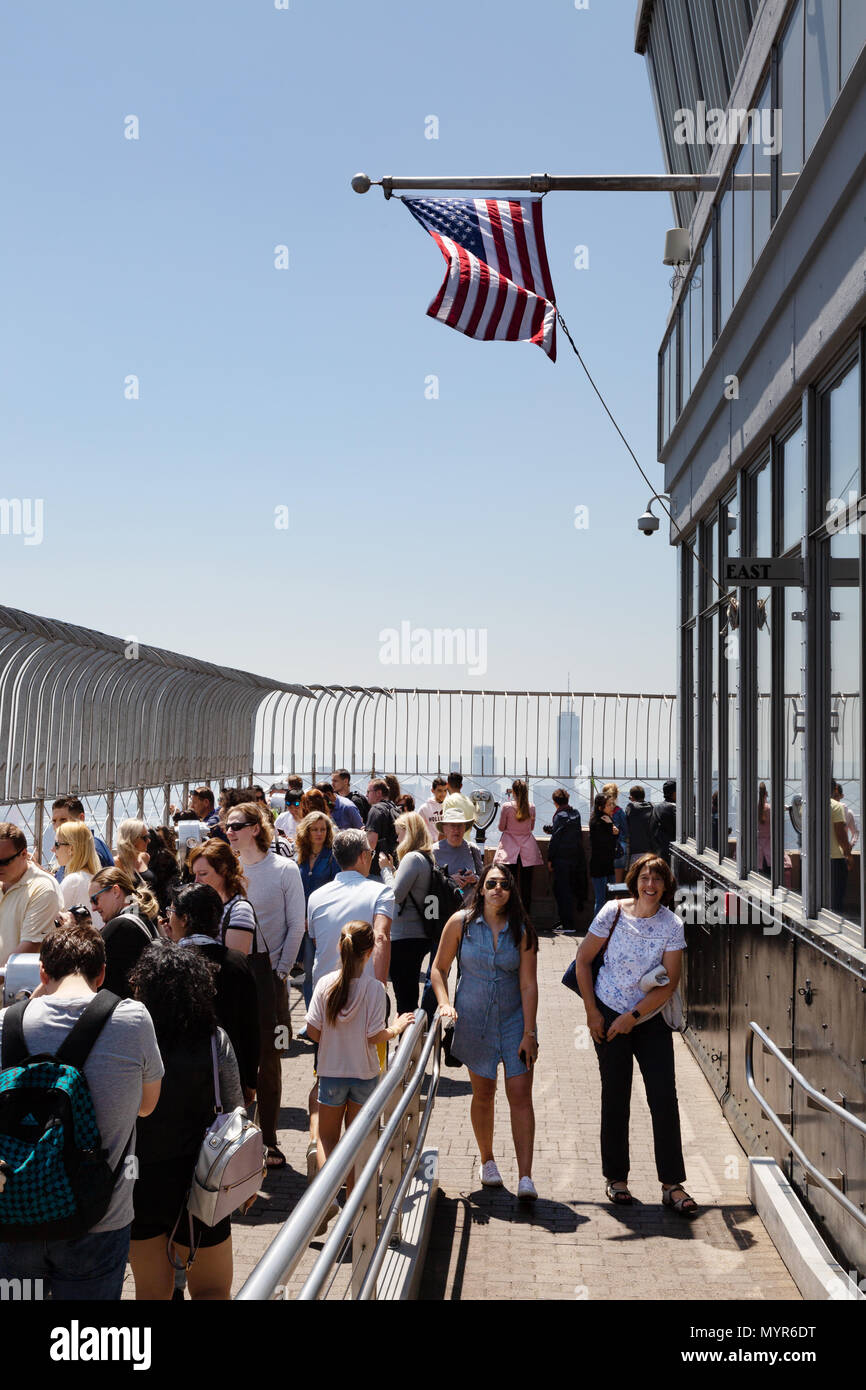 La folla di turisti in cima all'Empire State Building con la bandiera americana battenti, New York City, Stati Uniti d'America Foto Stock