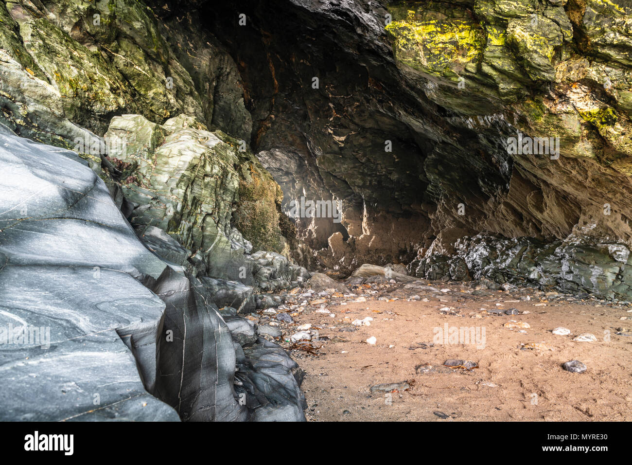 Un albero di luce brilla attraverso Merlin's Cave con la bassa marea. La grotta si trova sotto il castello di Tintagel in Cornovaglia del Nord ed è stato reso famoso da Te Foto Stock