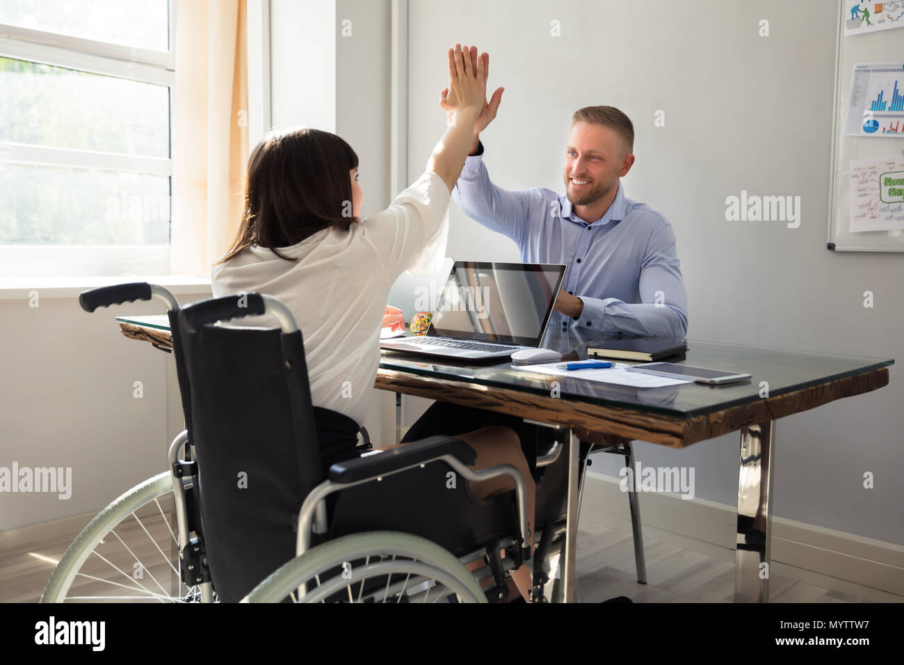 Imprenditrice disabili dando alta cinque al suo sorridente partner di sesso maschile in Office Foto Stock
