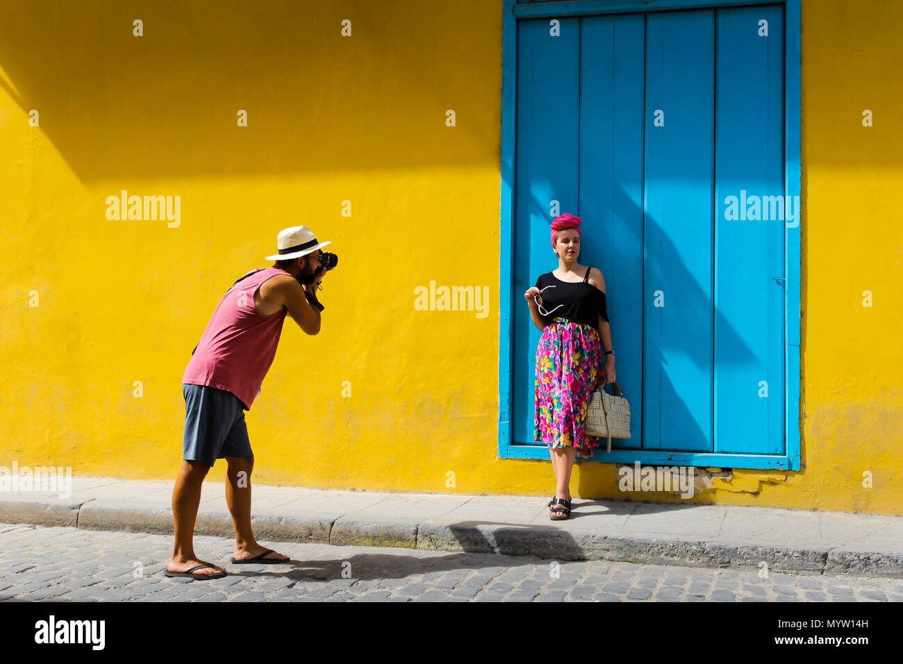Uomo di scattare una foto di una ragazza in Havana Cuba contro una parete di colore giallo Foto Stock
