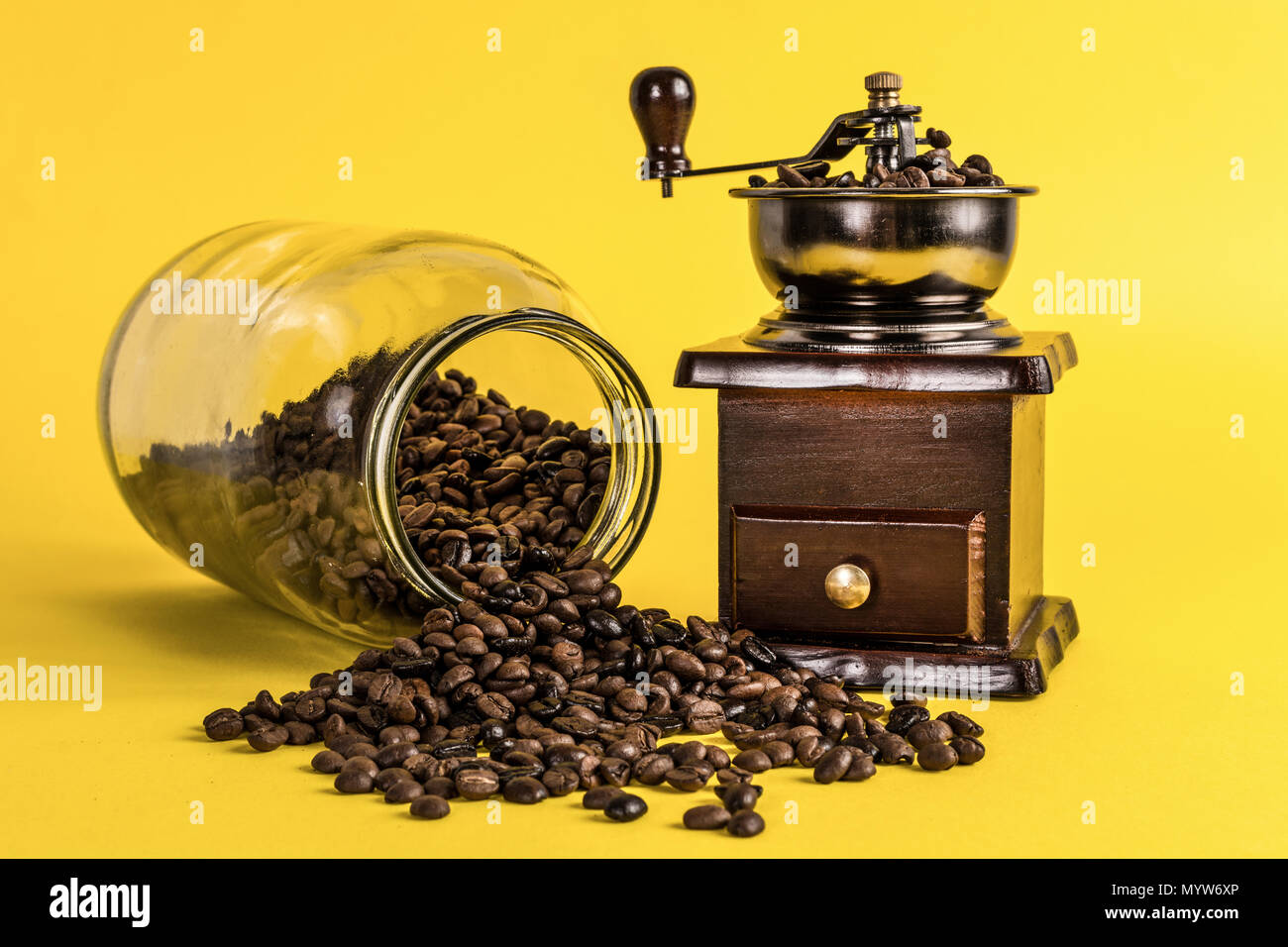 Macinino da caffè e versato fagioli arrosto dal barattolo di vetro giallo su sfondo rétro. Il cibo e le bevande concept Foto Stock