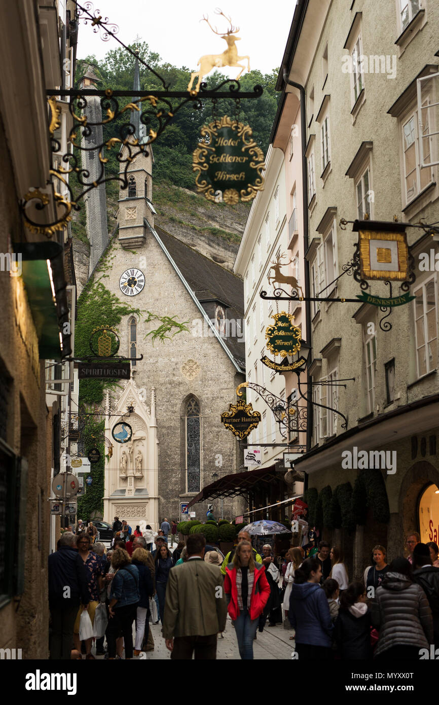 Gli amanti dello shopping a piedi giù per la Getreidegasse, la famosa via dello shopping nel centro di Salisburgo, Austria. La Chiesa di San Biagio Chiesa è in background. Foto Stock