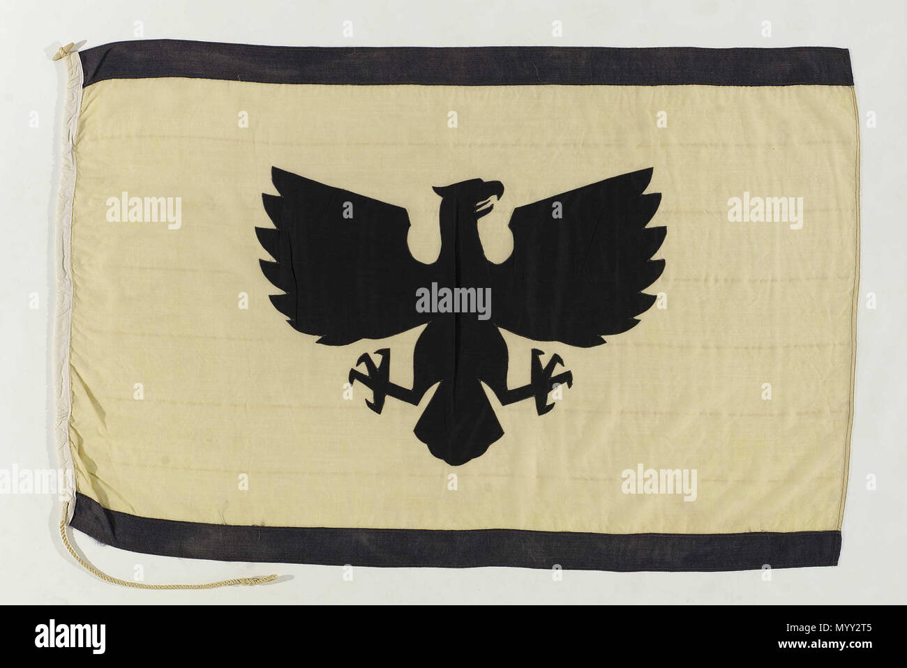 . Inglese: Casa bandiera, olio di Eagle Shipping Co. Ltd la casa bandiera di olio Eagle Shipping Co. Ltd, Londra. Un giallo bandiera rettangolare con una striscia nera attraverso i bordi di sommità e di fondo. Nel centro è un'aquila nera viene visualizzato. La bandiera è di lana bunting con un paranco di cotone. Si tratta di macchina cucito e l'aquila motif è realizzato in cotone. Una corda e alternare è allegata. La compagnia di navigazione è stato impostato per nave olio dal messicano campi olio per l'Europa. Le loro navi erano coinvolti in convogli mercantili durante le due guerre mondiali. Essi erano i proprietari della "Demetrio' reboarded dal suo equipaggio e salvato Foto Stock