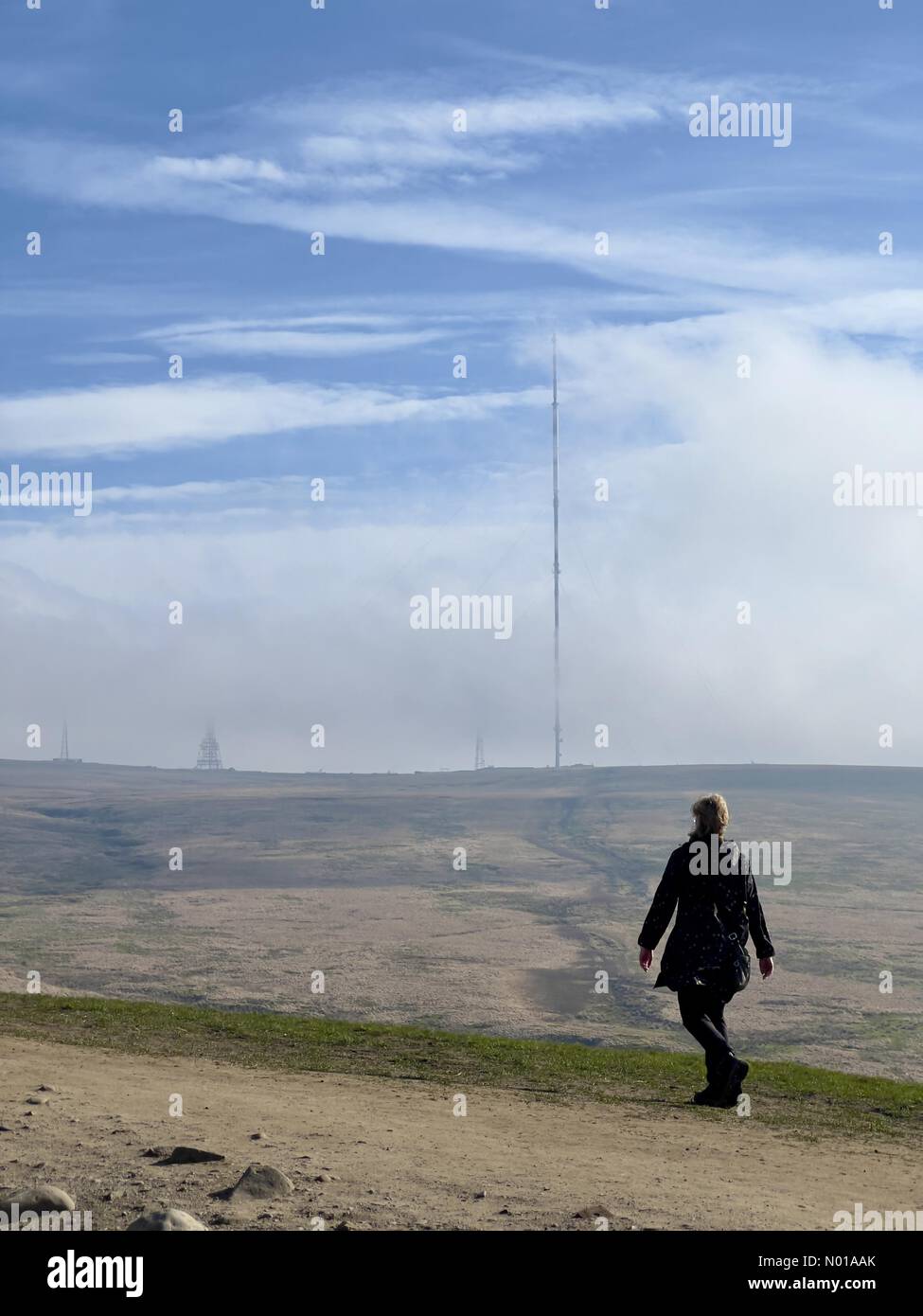 Meteo nel Regno Unito: Soleggiato a Rivington, Lancashire. Una domenica di Pasqua soleggiata a Rivington vicino Chorley nel Lancashire. Una mattinata ventosa in cima a Rivington Pike con una donna che cammina e l'albero TV di Winter Hill Foto Stock