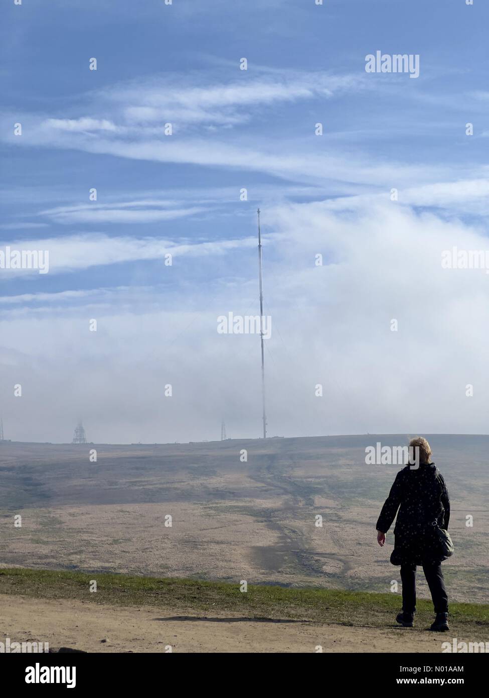 Meteo nel Regno Unito: Soleggiato a Rivington, Lancashire. Una domenica di Pasqua soleggiata a Rivington vicino Chorley nel Lancashire. Una mattinata ventosa in cima a Rivington Pike con una donna che cammina e l'albero TV di Winter Hill. Foto Stock