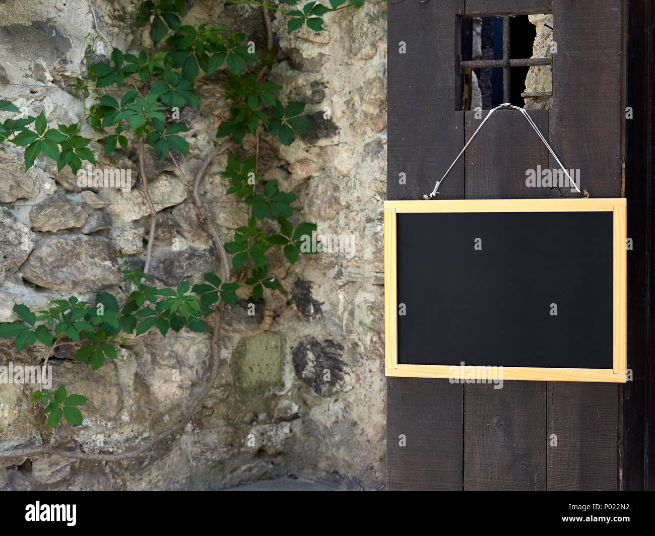 Vista del raccolto di muro di pietra con impianti e scuri in legno porta con scheda di iscrizione Foto Stock