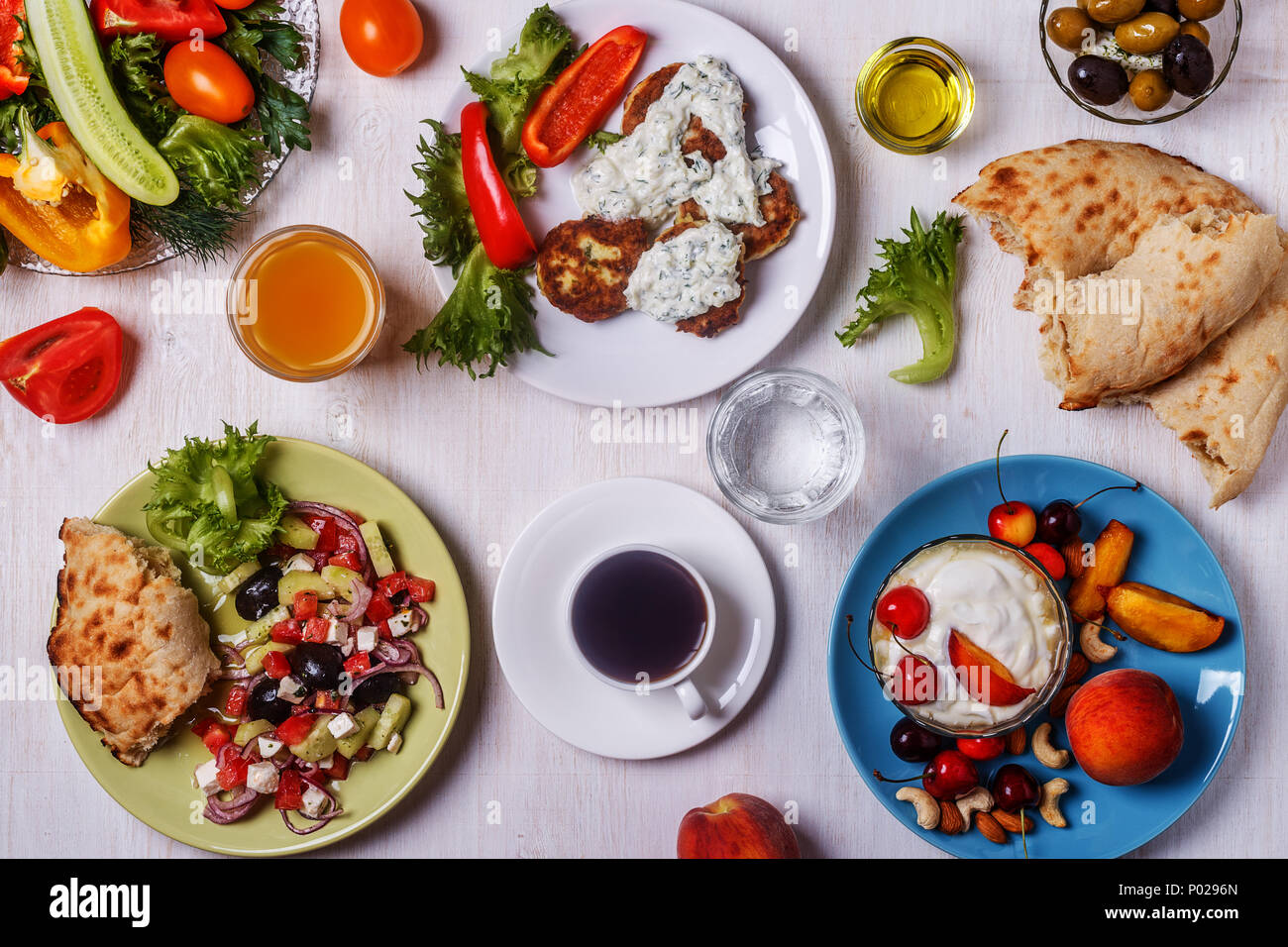 Antipasti di greco - le frittelle di zucchine con salsa tzatziki, insalata greca, yogurt con frutta fresca e secca, olive, le verdure e le erbe aromatiche, vista dall'alto. Foto Stock