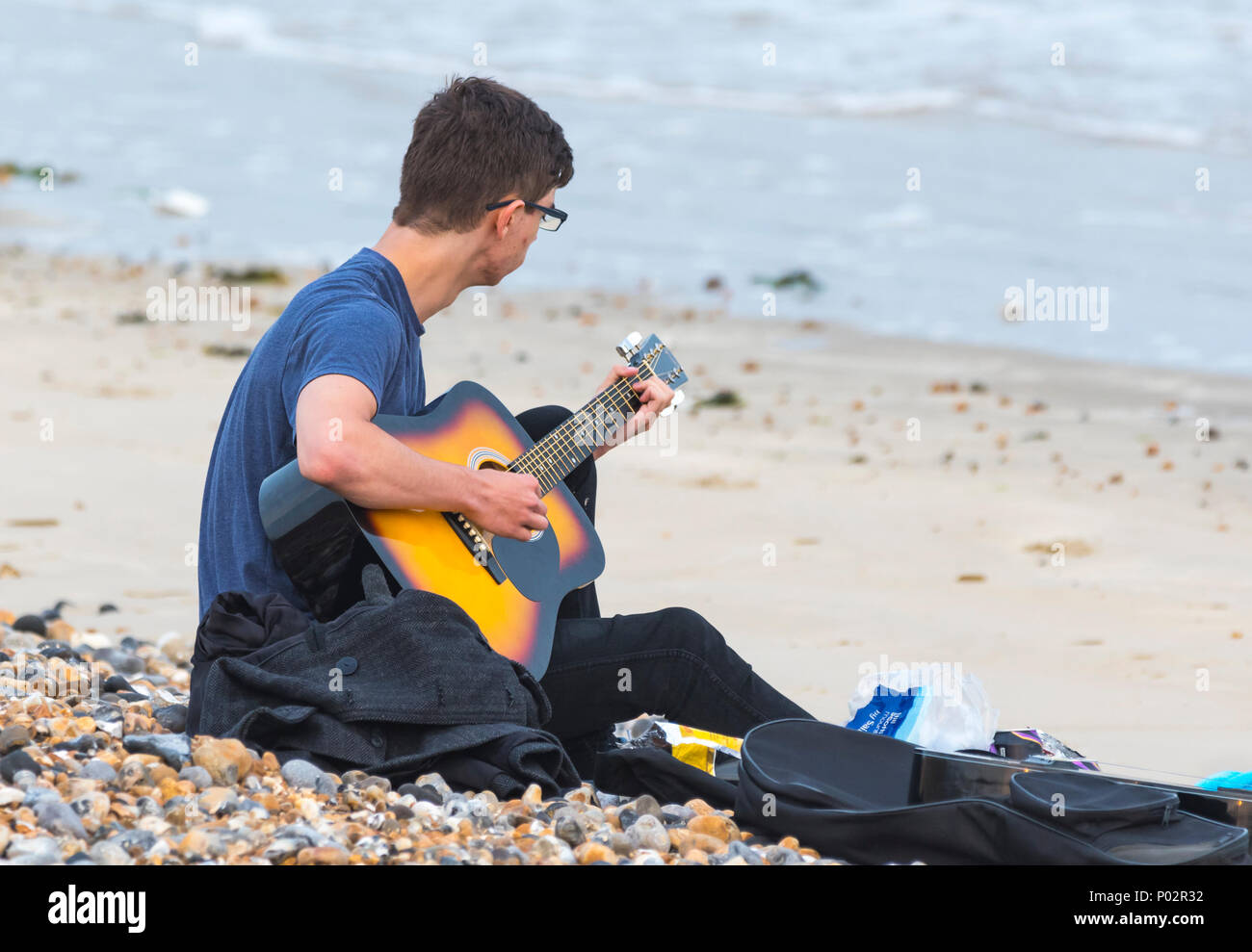 Giovane uomo seduto su di una spiaggia di sabbia di suonare una chitarra, NEL REGNO UNITO. Foto Stock