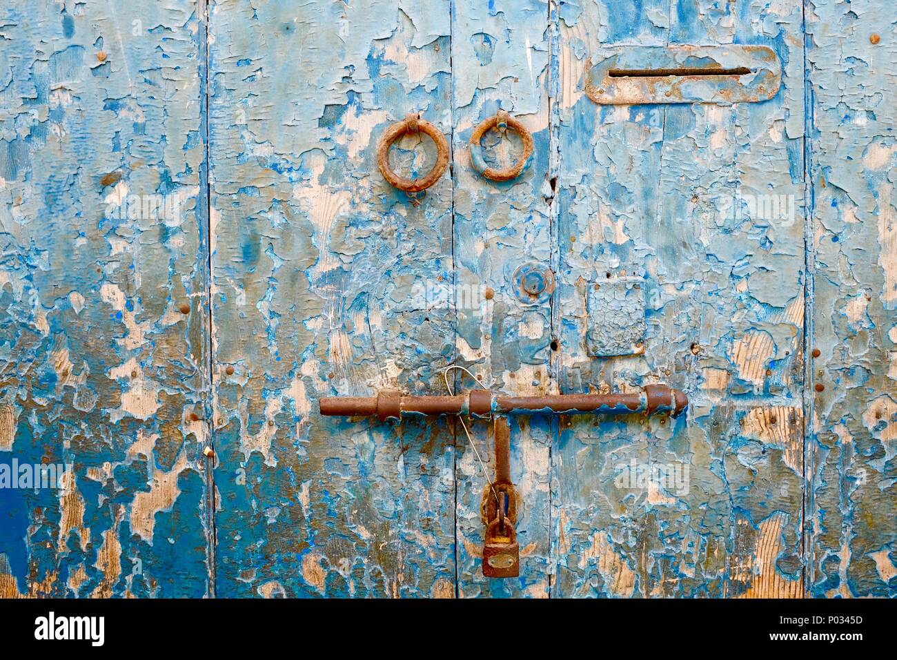 Close up peeling usurato porta in legno verniciato blu vibranti con lucchetto arrugginito e letterbox. Ampio lo spazio editoriale Foto Stock