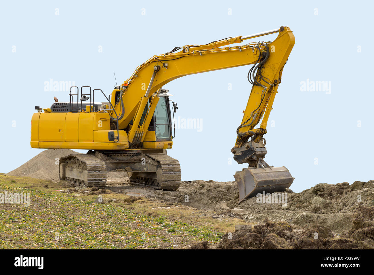 Escavatore giallo a argilloso sito in costruzione, parzialmente isolato in azzurro indietro Foto Stock