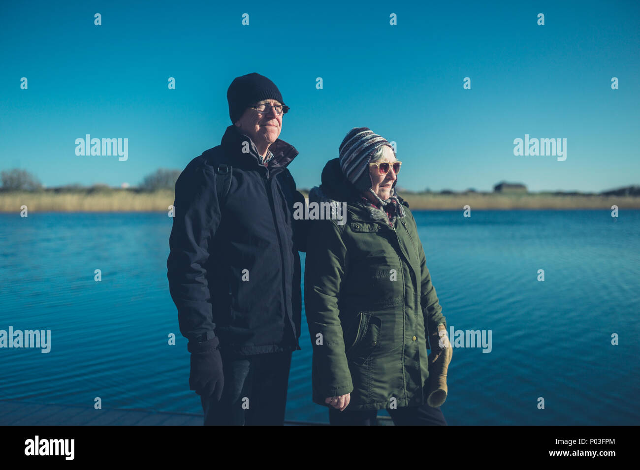 Una coppia senior sono in piedi dall'acqua su una soleggiata giornata invernale Foto Stock