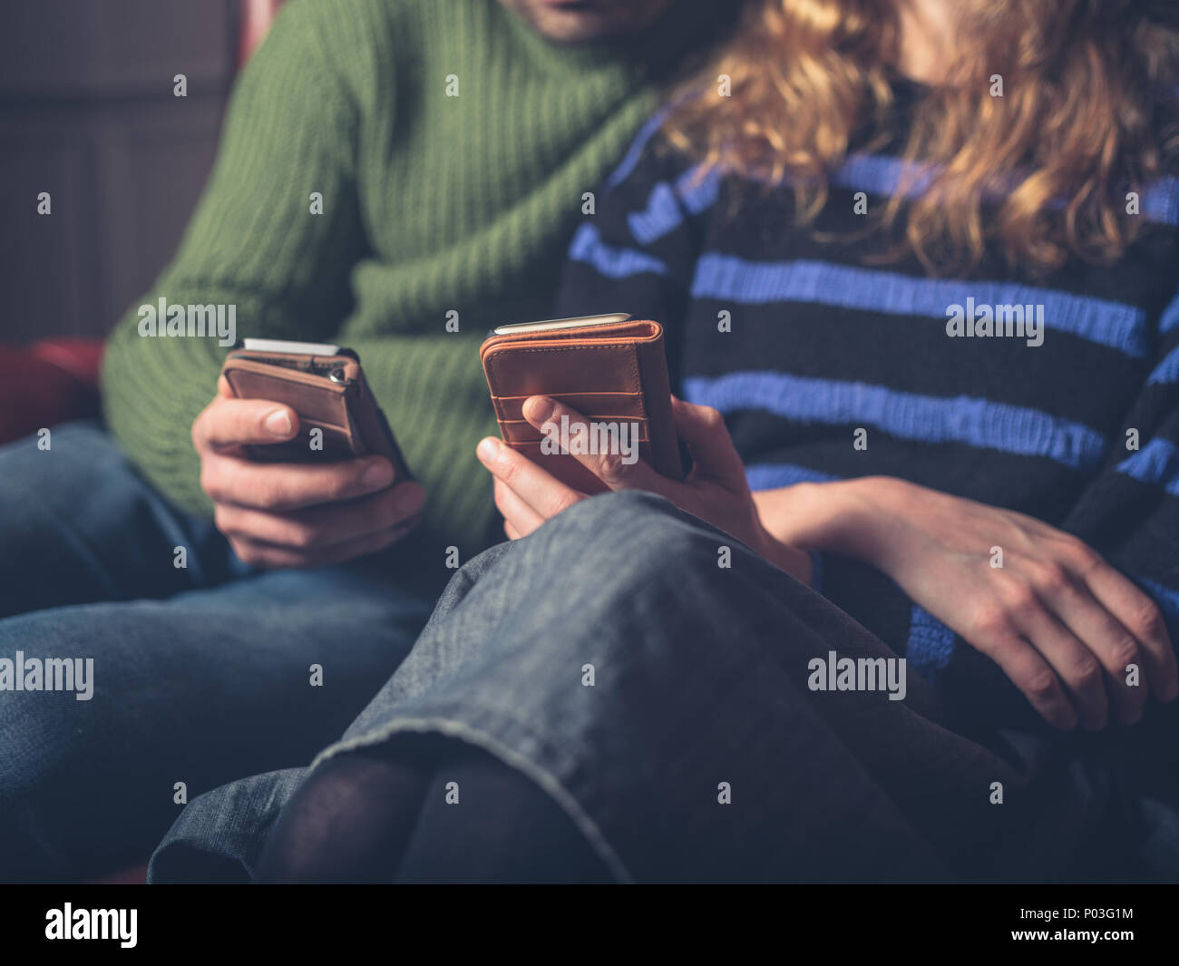 Un uomo e una donna sono seduti su un divano utilizzando i loro telefoni intelligenti Foto Stock