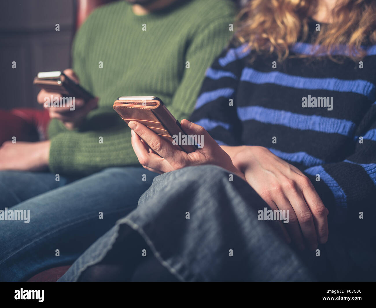 Un uomo e una donna sono seduti su un divano utilizzando i loro telefoni intelligenti Foto Stock