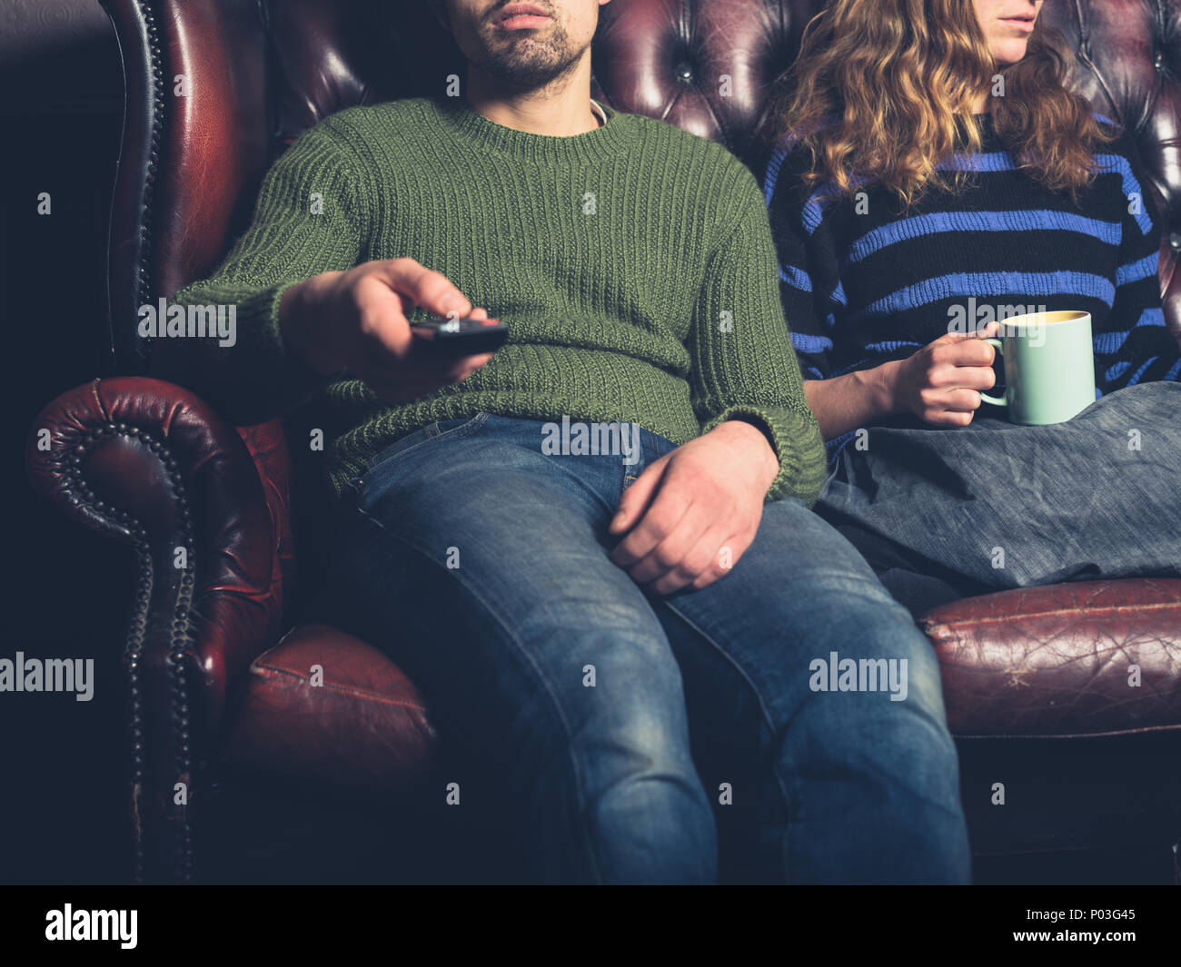 Un annoiato coppia giovane sono seduto su un divano a casa a guardare la televisione Foto Stock