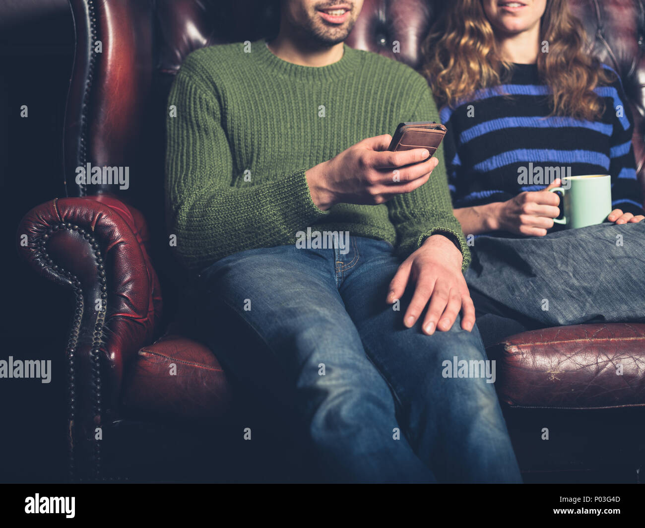 Un giovane uomo su un divano sta mostrando la sua fidanzata qualcosa sul suo telefono cellulare Foto Stock