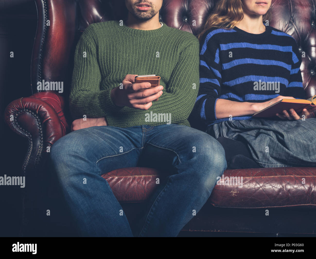 Una giovane coppia su un divano a casa sono leggere e utilizzando un telefono cellulare Foto Stock