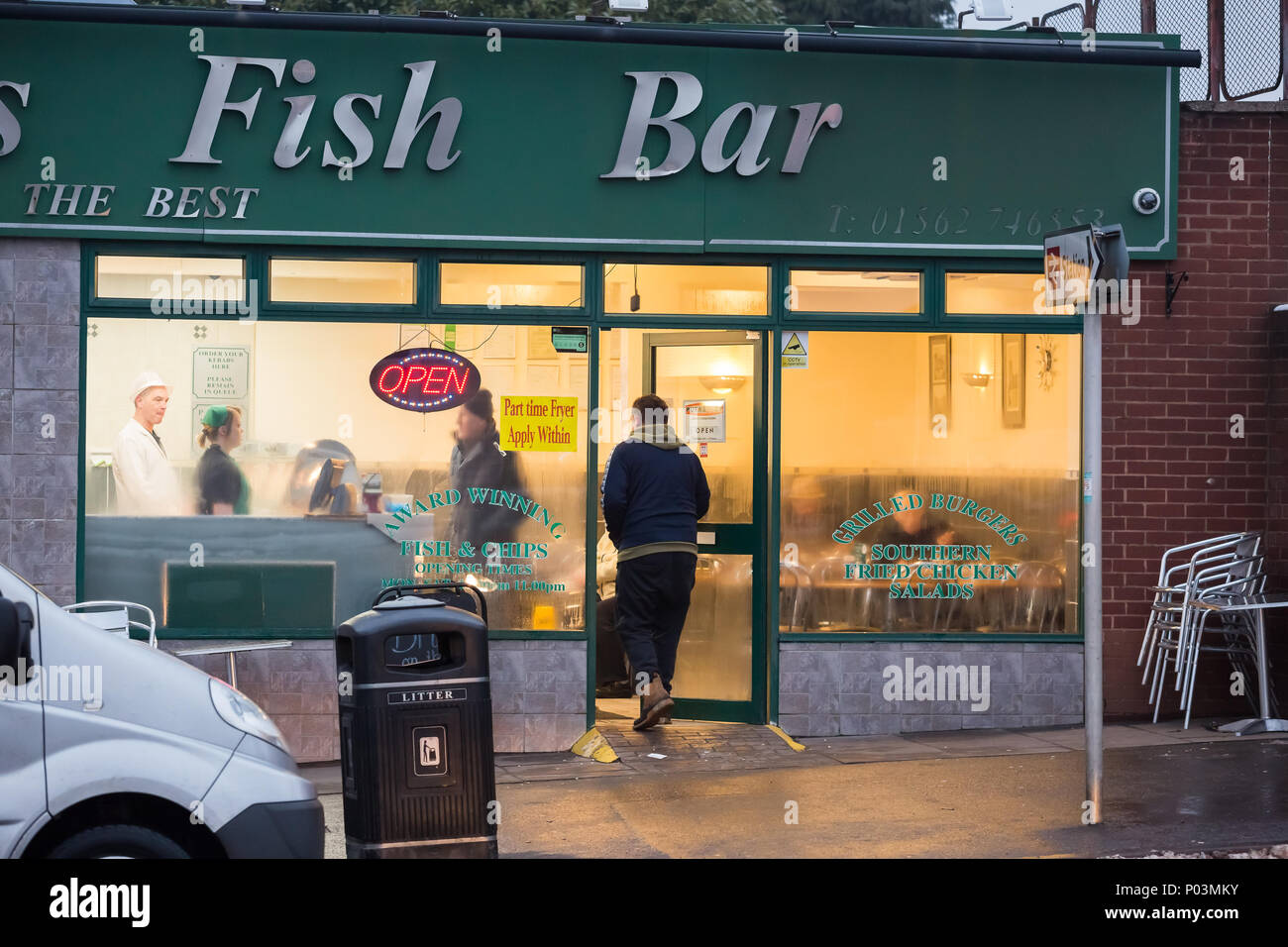 Negozio di fish & chip britannico, aperto per gli affari. Il cliente apre la porta per ritirare il cibo da asporto, un altro cliente si siede all'interno e mangia all'interno dell'hotel. Foto Stock