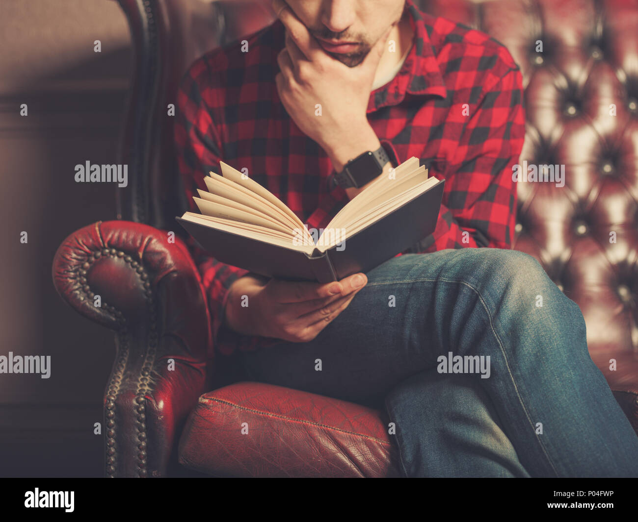 Un giovane uomo seduto su un divano in pelle è la lettura di un libro Foto Stock