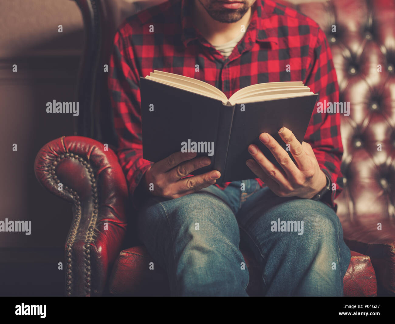 Un giovane uomo seduto su un divano in pelle è la lettura di un libro Foto Stock