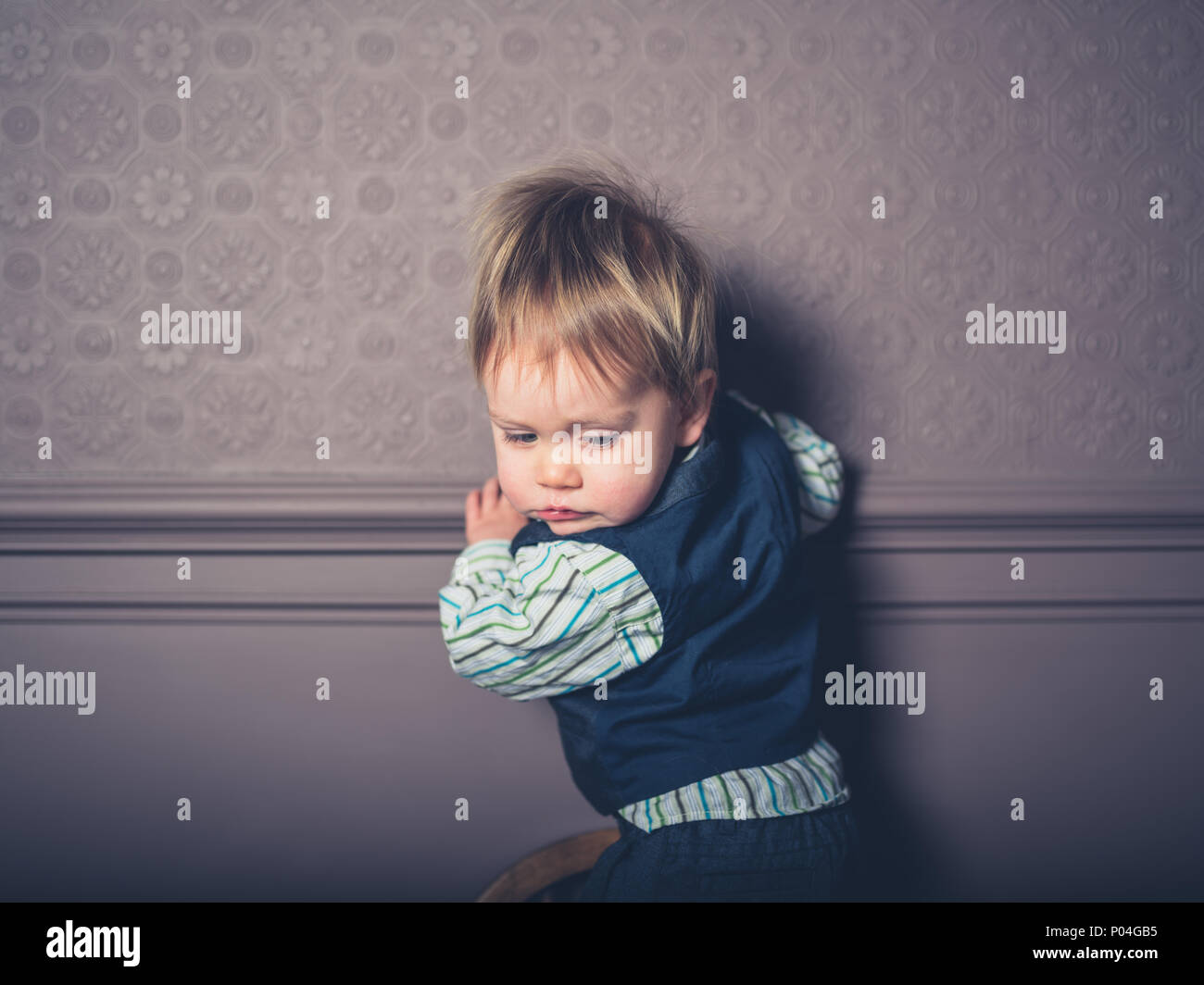 Un grazioso piccolo ragazzo è in piedi su una sedia in un lussuoso soggiorno Foto Stock