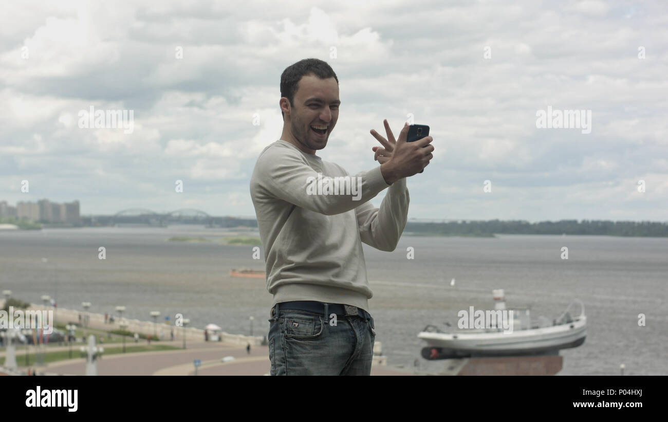 Giovane fa selfie con il telefono cellulare vicino al fiume sul giorno nuvoloso Foto Stock