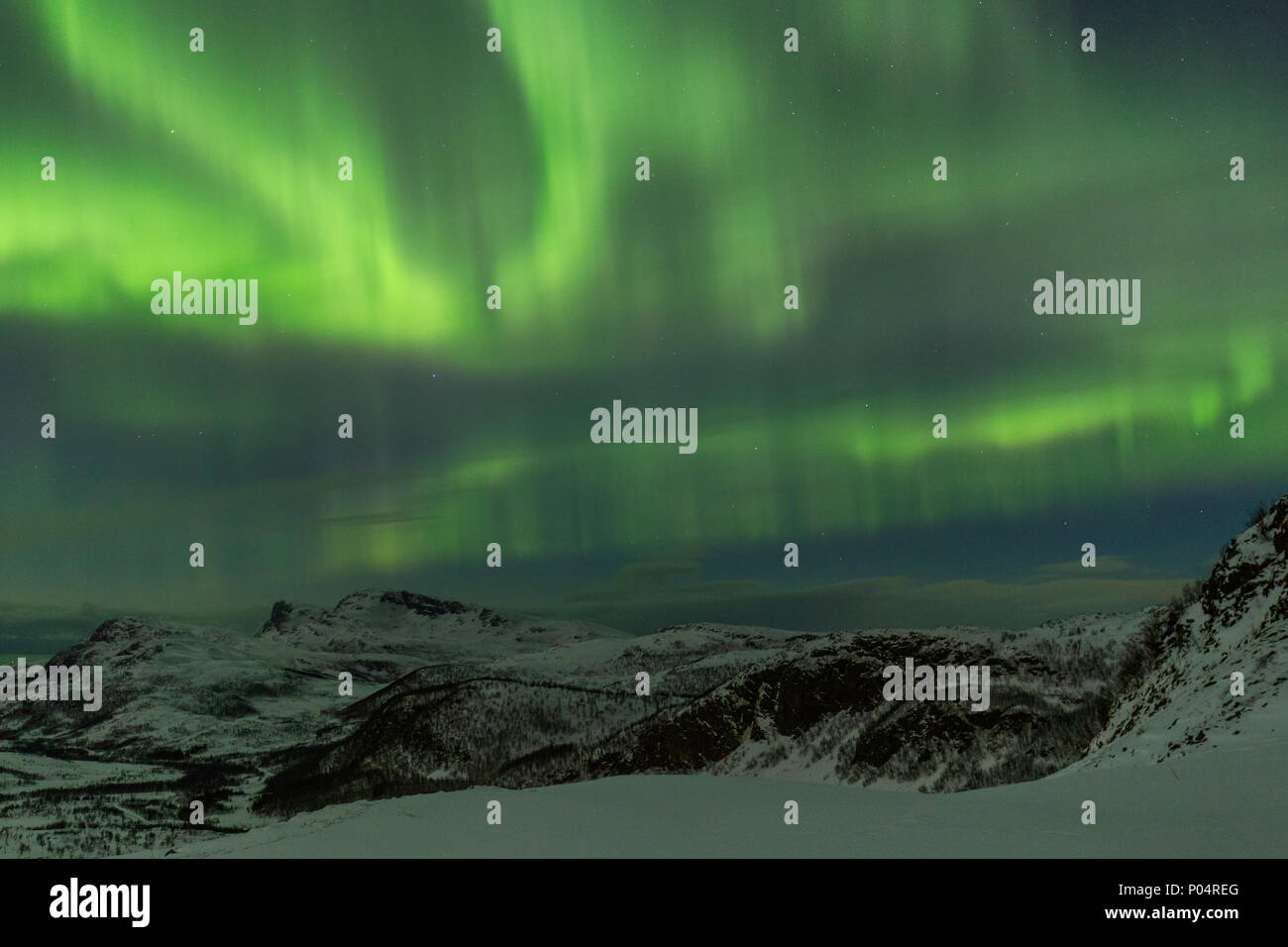 Luci del nord su montagne coperte di neve a distante Norvegia costa. Molto luminosa aurora boreale riempie tutto il cielo artico Foto Stock