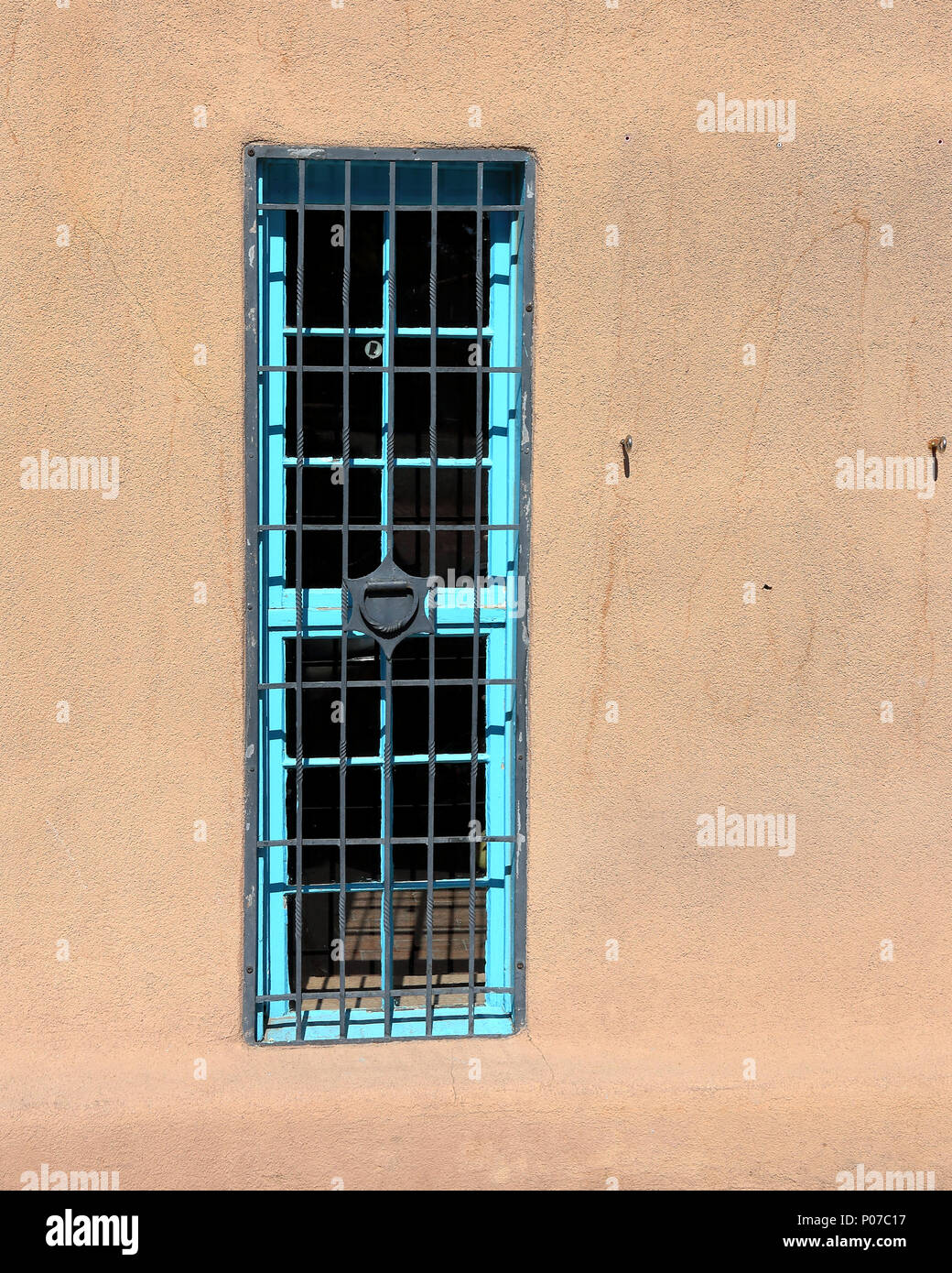 Una singola finestra blu con barre su una parete di adobe Foto Stock
