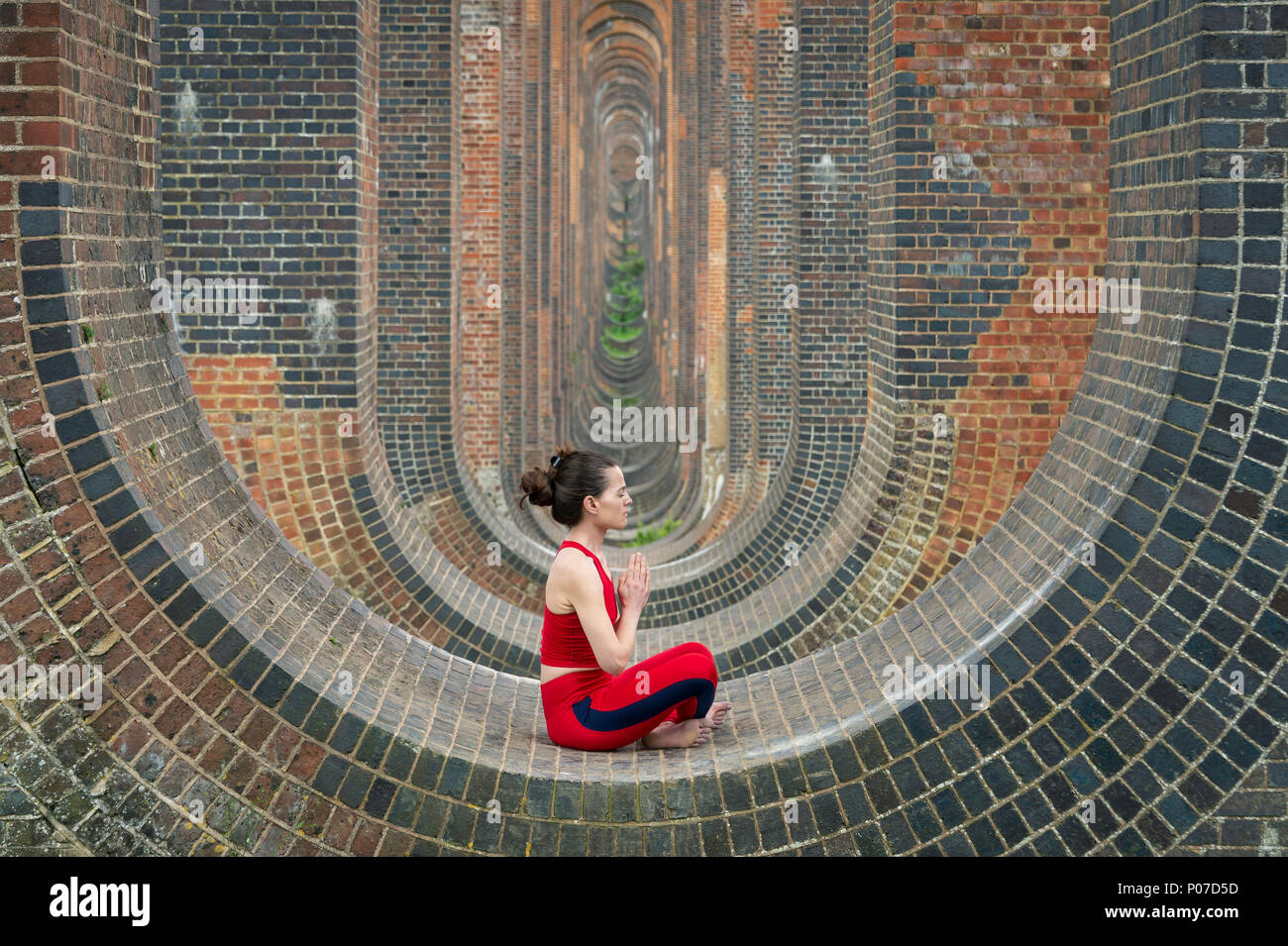 Donna seduta negli archi del Ouse Valley viadotto a praticare yoga e meditazione Foto Stock