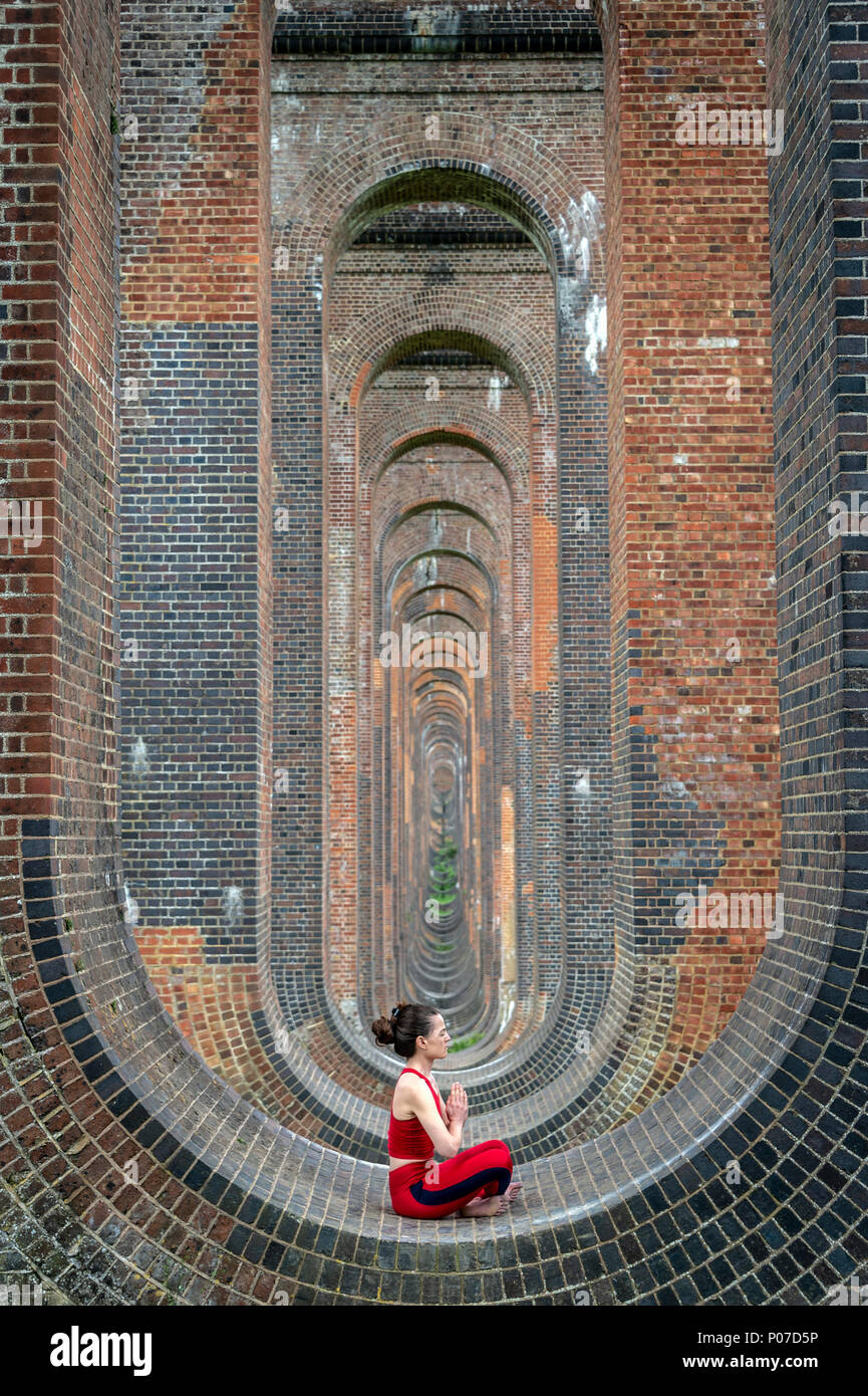 Donna seduta negli archi del Ouse Valley viadotto a praticare yoga e meditazione Foto Stock