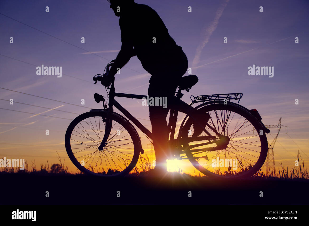 Man comando di avviamento sulla bicicletta. Silhouette del ciclista sulla bici retrò con il cielo al tramonto e campo energetico in background Foto Stock