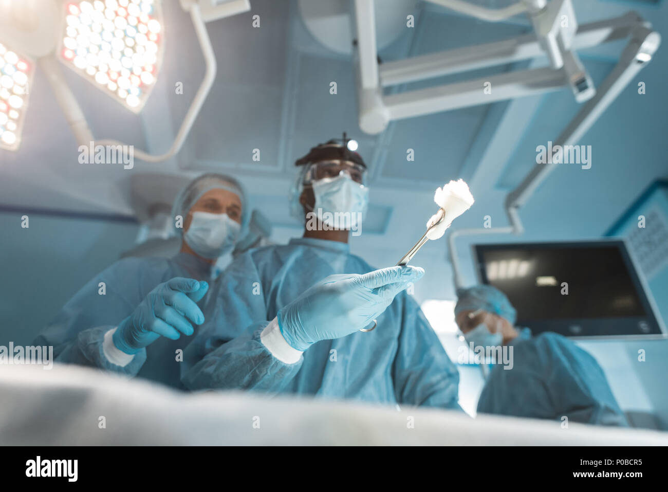 Vista dal basso dei chirurghi multiculturale con strumenti durante la chirurgia Foto Stock